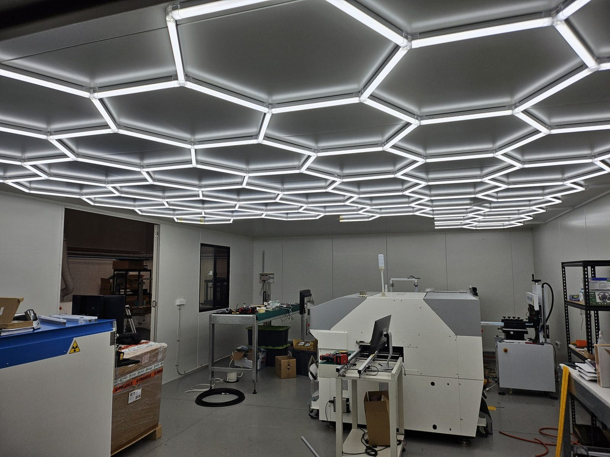 Fabrication workshop with workbenches and machinery lit by a large HEXA hexagon LED panel grid